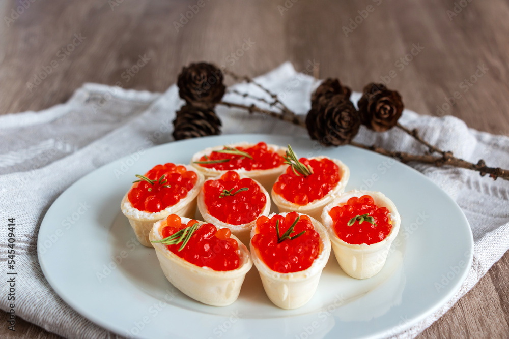 Red caviar in a waffle tartlet on a white plate with a linen napkin on a wooden background Red caviar in a waffle tartlet on a white plate with a linen napkin on a wooden background