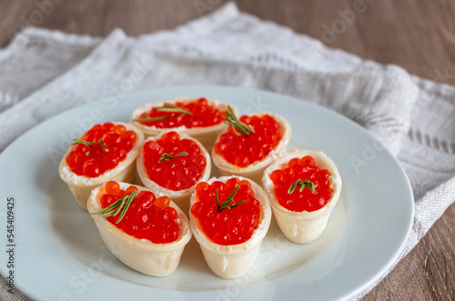 Red caviar in a waffle tartlet on a white plate with a linen napkin on a wooden background