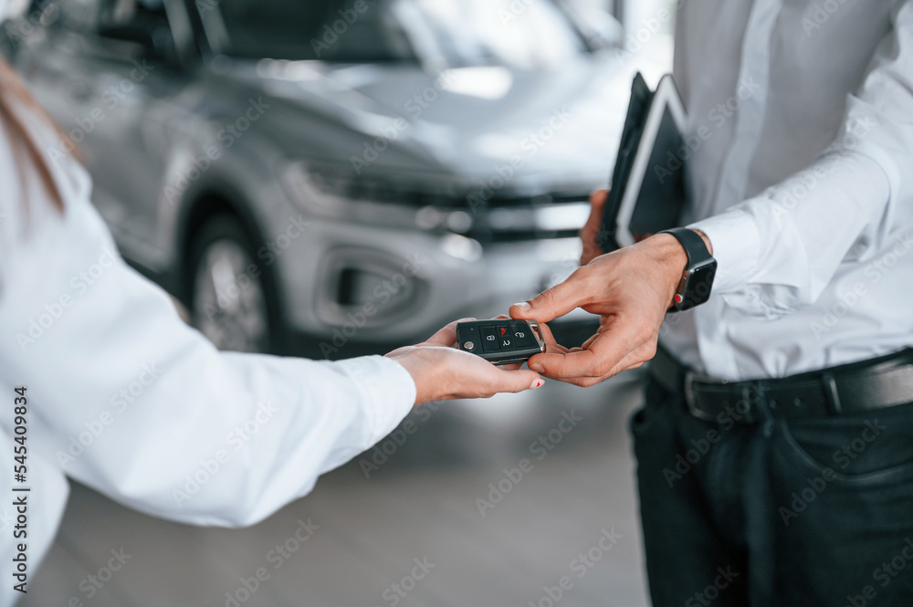 Keys of new automobile. Close up view. Man with woman in white clothes are in the car dealership together