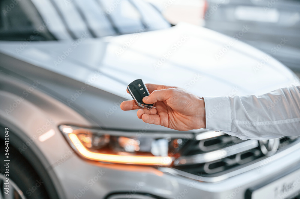 Naklejka premium Keys and remote controller. Close up view. Young man in white clothes is in the car dealership