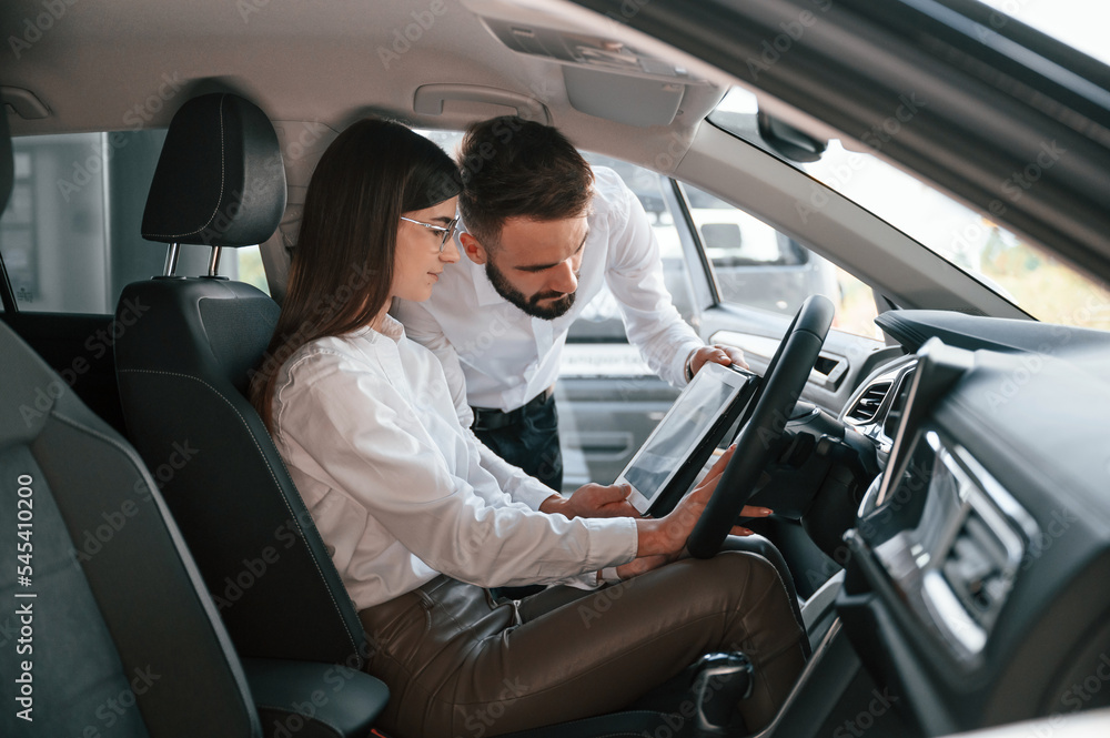 Sitting in the automobile. Man with woman in white clothes are in the car dealership together Sitting in the automobile. Man with woman in white clothes are in the car dealership together