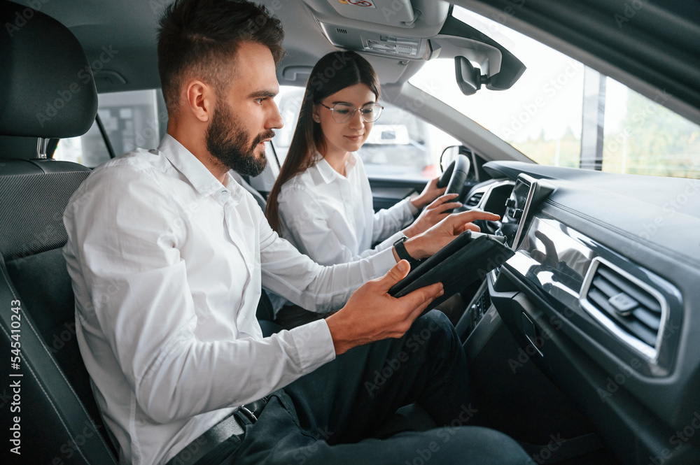 Sitting in the automobile. Man with woman in white clothes are in the car dealership together Sitting in the automobile. Man with woman in white clothes are in the car dealership together