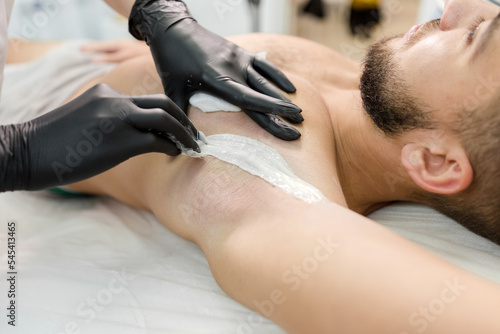 Girl cosmetologist makes hair removal on the armpit of a man