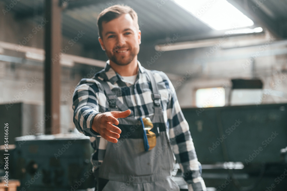 Friendly factory male worker in uniform is indoors giving hand Friendly factory male worker in uniform is indoors giving hand