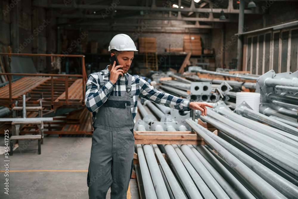 Talking by phone. Factory male worker in uniform is indoors Talking by phone. Factory male worker in uniform is indoors