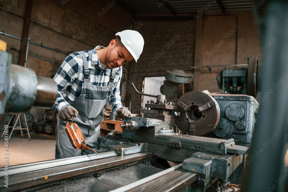Side view. Using machine. Factory male worker in uniform is indoors Side view. Using machine. Factory male worker in uniform is indoors