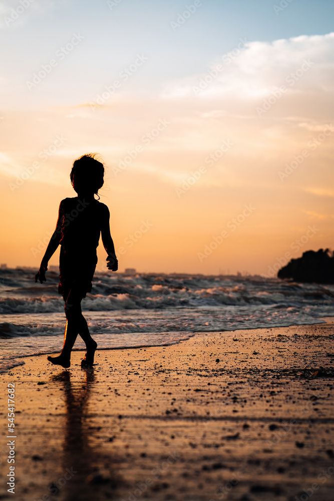 silhouette of a child walking by the beach during golden sunset.