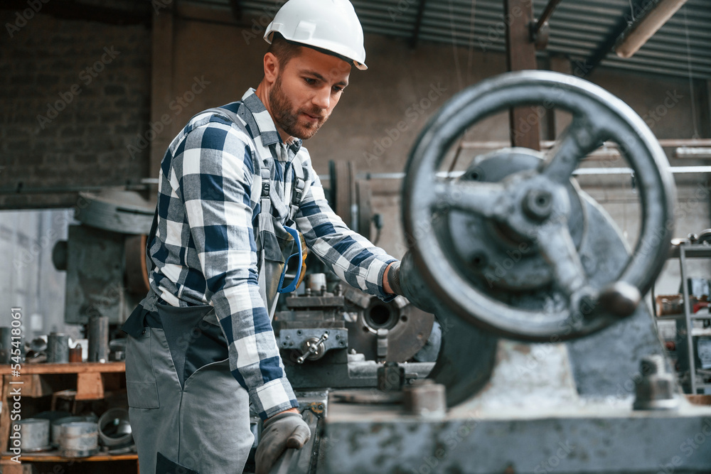 Factory male worker in uniform is indoors. With industry machine Factory male worker in uniform is indoors. With industry machine