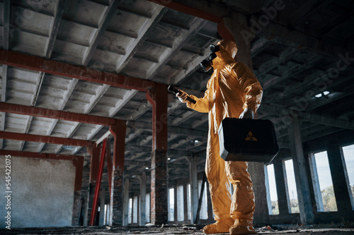 Indoors with flashlight. Man dressed in chemical protection suit in the ruins of the post apocalyptic building