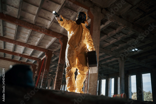 Using the flashlight. Man dressed in chemical protection suit in the ruins of the post apocalyptic building © standret