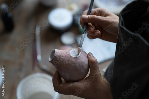 Craftsmaster draws symbol on clay pitcher wanting to decorate kitchen with utensils. Lady master using pencil makes sketch to bring to life and creates new masterpiece for exhibition putting effort photo