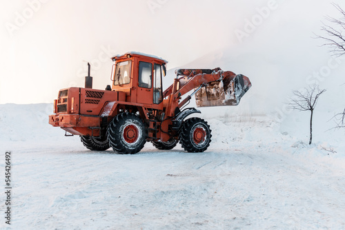 A bulldozer removes snow with an iron bucket after a blizzard. Cleaning snowdrifts with a bulldozer. Cleaning the city after a blizzard.