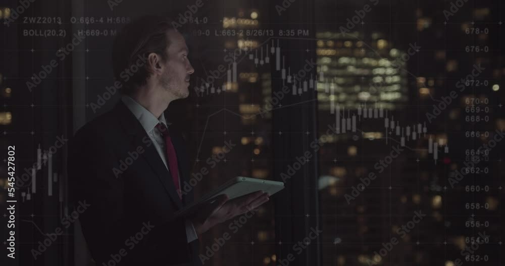Businessman Working Late Looking at Digital Tablet in Office with Graph and Skyline Businessman Working Late Looking at Digital Tablet in Office with Graph and Skyline