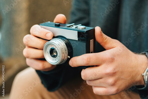 Strong hands of a young man are holding a vintage photo camera in street.