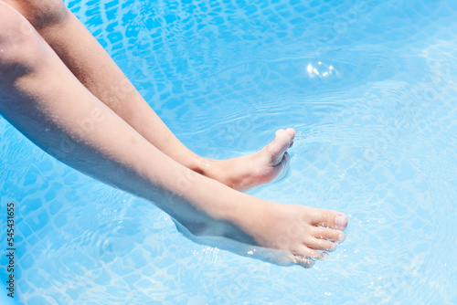someone's feet in the water with their toes sticking to the edge of a swimming pool, which is blue and clear