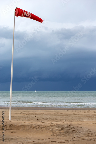 Red and white windsock indicator on blue sky with many white clouds background