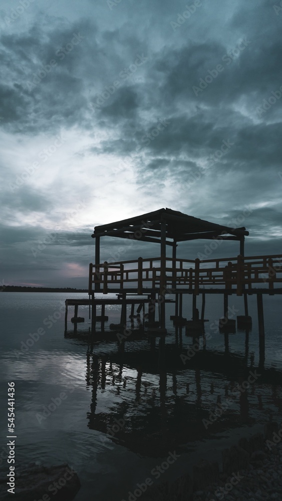 Vertical shot of a jetty over a calm lake against a cloudy sky