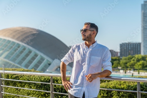 Hispanic man with white shirt and glasses leaning on a railing posing in the city of Valencia, Spain photo