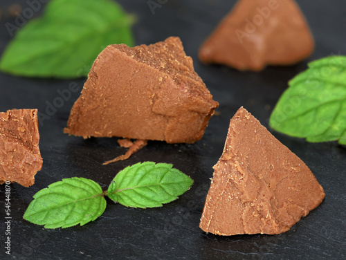 Sweet chocolate hazelnut nougat pieces with mint leaves isolated on black slate board, as baking ingredient or sweet spread