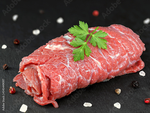 single raw unfilled beef roulade with salt and peper on black slate board, traditional german food