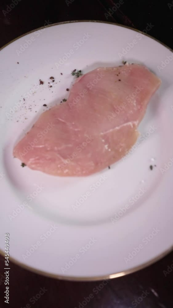 Vertical shot of a chef seasoning a raw piece of chicken meat on a plate Vertical shot of a chef seasoning a raw piece of chicken meat on a plate