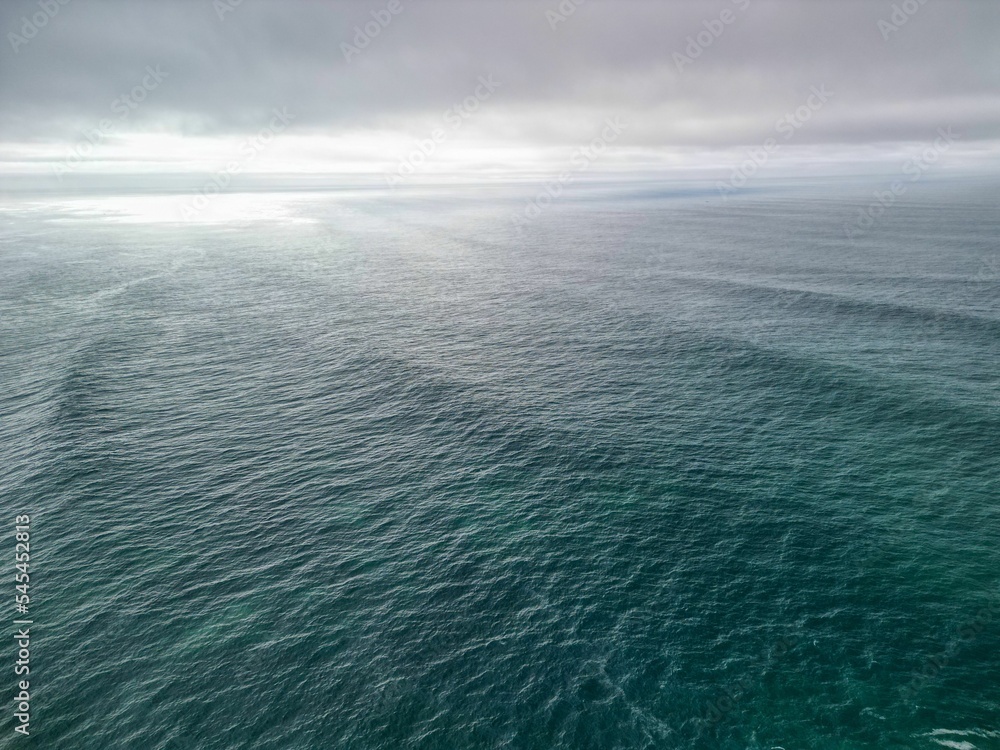 Drone shot over the blue water with a gray cloudy sky