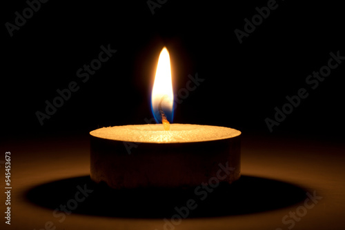 single burning warm candle or tealight close-up in the dark