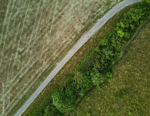 Aerial shot of symmetrical road separating patterned fields and a green meadow covered with trees
