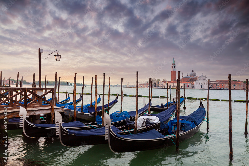 A row of gondolas parked beside the Riva degli Schiavoni in Venice, Italy. View of the Venetian Lagoon. The Church of San Giorgio Maggiore on island of the Venice, Italy, Europe