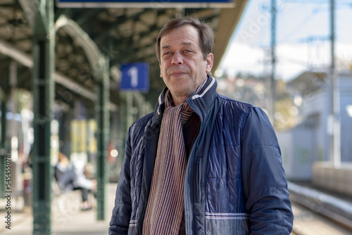Street portrait of a man 45-50 years old on the platform of a railway station in Europe, waiting for a train or commuter train.