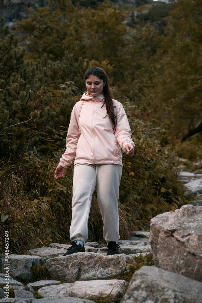 Woman hiker on the top of the mountain. Concept of adventure vacations. Traveler millennial girl is staying on the cliff edge with autumn forest and enjoying beautiful valley view. Woman hiker on the top of the mountain. Concept of adventure vacations. Traveler millennial girl is staying on the cliff edge with autumn forest and enjoying beautiful valley view.