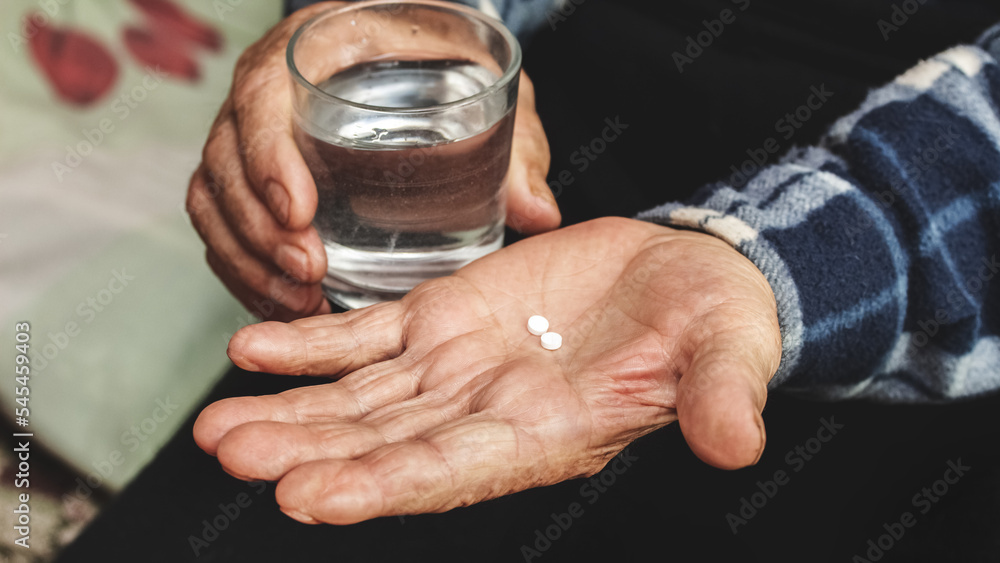 An elderly man holds pills and a glass of water in his hands. Taking pills to treat the disease