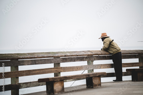 Foto Adult man fishing, leaned against a wooden handrail on a foggy day