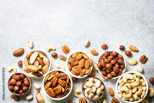 Assortment of nuts in the bowls. Cashew, hazelnuts, pecan, almonds, brazilian nuts and pistachios at light stone table. Top view with copy space.