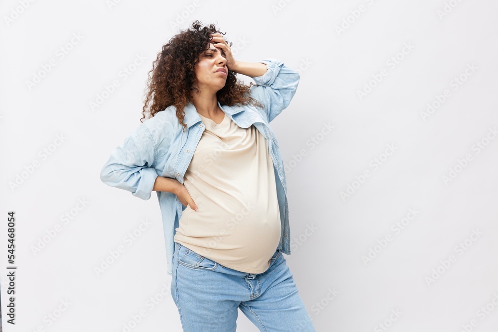 Pregnant woman tired, headache and abdominal pain, heavy pregnancy, last month before childbirth on white isolated background in T-shirt with blue shirt Pregnant woman tired, headache and abdominal pain, heavy pregnancy, last month before childbirth on white isolated background in T-shirt with blue shirt