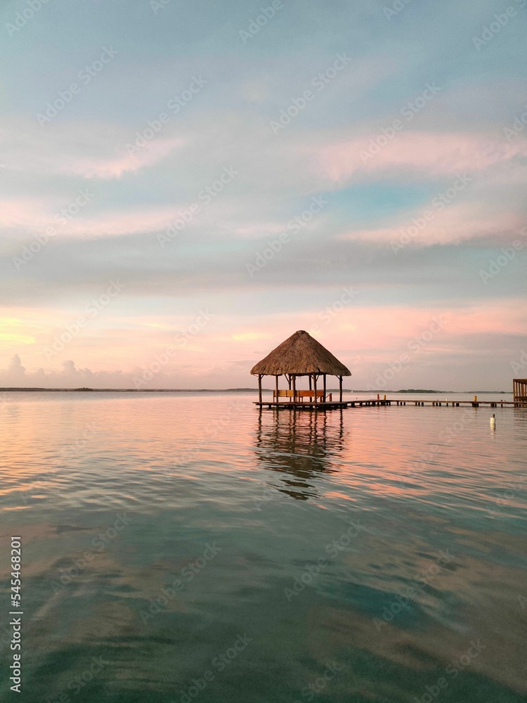 View of a sunset from lake Bacalar with a red and blue skyline and woody bridge, a roof in the water View of a sunset from lake Bacalar with a red and blue skyline and woody bridge, a roof in the water