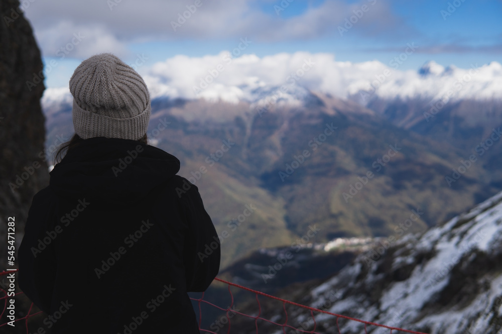 Adult girl stand close to cliff, snow mountains and blue sky with white clouds background. mountain tourism and extreme trakking Adult girl stand close to cliff, snow mountains and blue sky with white clouds background. mountain tourism and extreme trakking