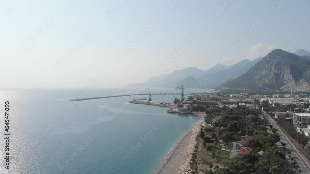 The camera flies over an industrial warehouse area on the coast of the sea near the mountains, where trucks drive on the roads. Seaport near the industrial zone. High quality 4k footage The camera flies over an industrial warehouse area on the coast of the sea near the mountains, where trucks drive on the roads. Seaport near the industrial zone. High quality 4k footage