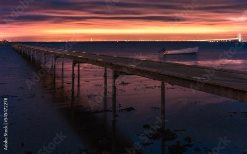 Fototapeta Naklejka Na Ścianę i Meble -  Mesmerizing shot of a sea pier and the colorful sunset giving a yellow-orange tinge to the sky