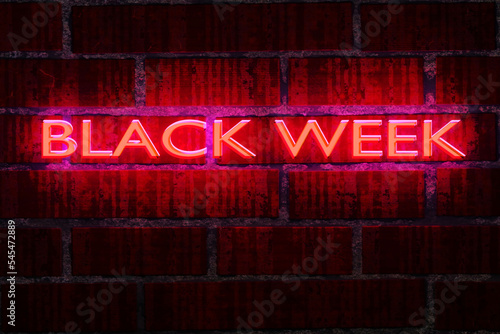 Black Friday concept. Neon Black Week text banner on grunge dark brick wall background.