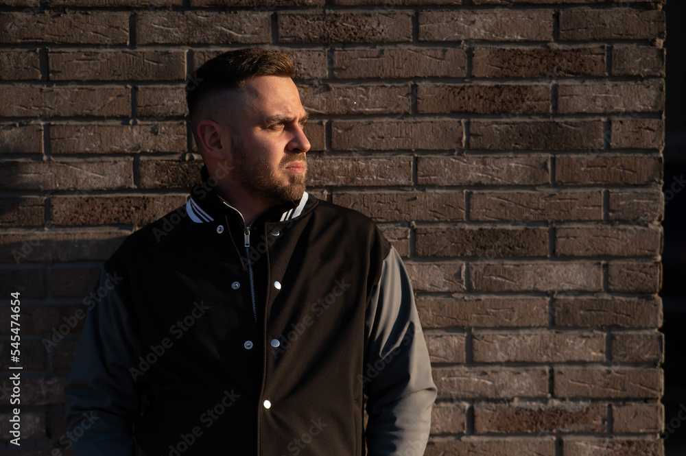 Caucasian bearded man in a bomber jacket leaned against a brick wall. Caucasian bearded man in a bomber jacket leaned against a brick wall.