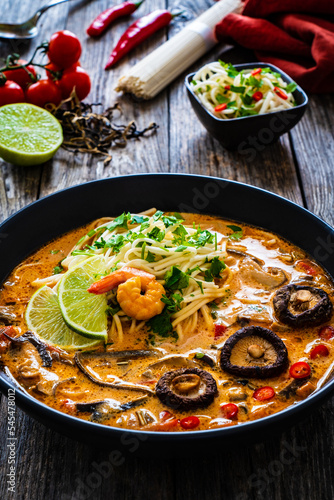 Tom Yum - Thai soup with prawn, shiitake mushrooms and noodles on wooden table
