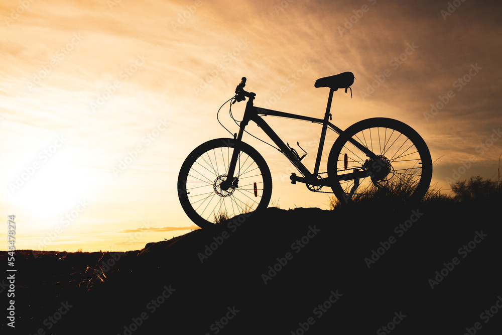 silhouette of a bicycle standing on a hill, the background is an orange sky with blurry clouds silhouette of a bicycle standing on a hill, the background is an orange sky with blurry clouds