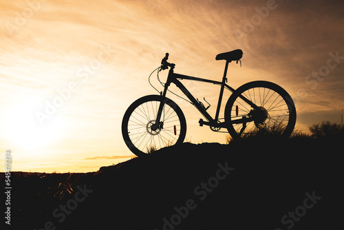 Fototapeta Naklejka Na Ścianę i Meble -  silhouette of a bicycle standing on a hill, the background is an orange sky with blurry clouds