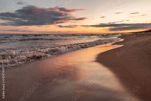 Orange sunset on the seashore, waves with golden sand.