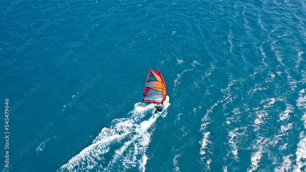 Aerial frone view photo of fit man practising wind surfing in Mediterranean bay with crystal clear deep blue sea Aerial frone view photo of fit man practising wind surfing in Mediterranean bay with crystal clear deep blue sea