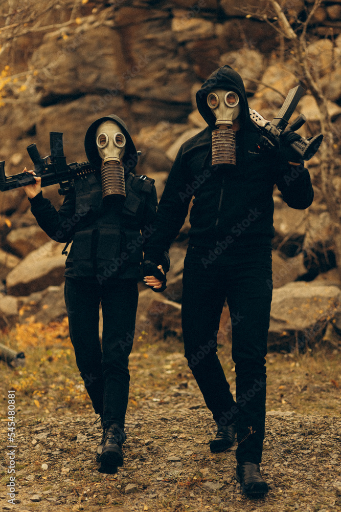 Guy and girl military in gas masks and with machine guns pose for camera.