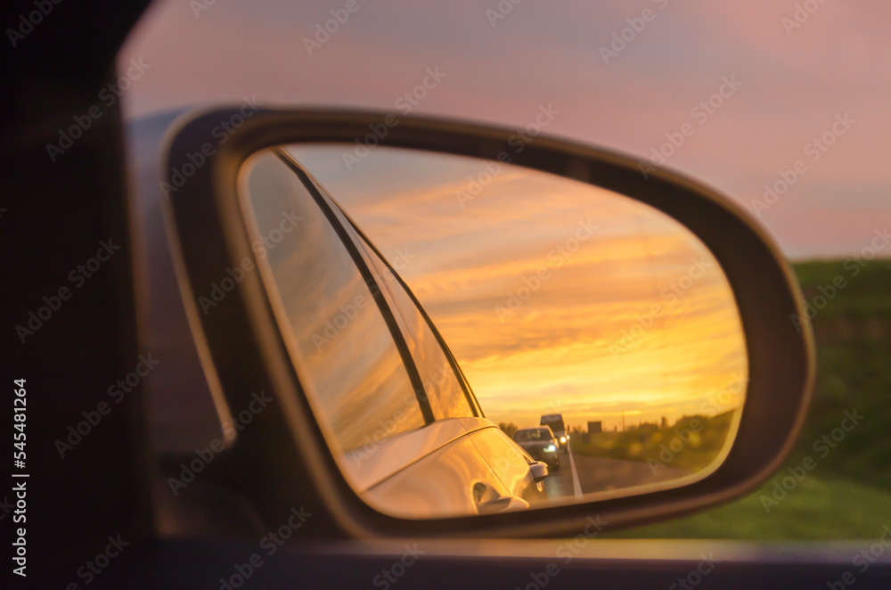 View in the rear view mirror on a road during a very colorful sunset