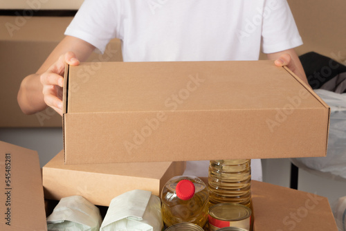 Teenage boy hands holding blank cardboard box. Volunteer collecting food into donation box. Donation, charity, food bank, help for low income, poor families, migrants, refugee, homeless people
