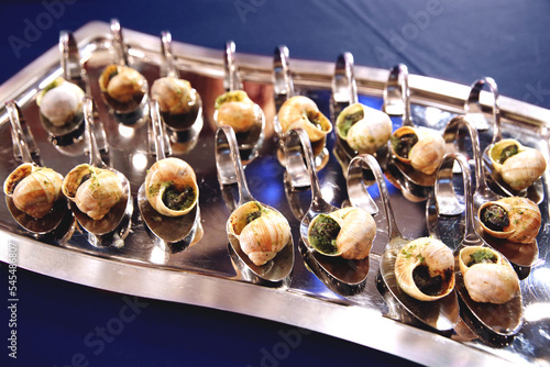 Escargots de Bourgogne.  Baked snails with garlic. French traditional food. Catering banquet. Table with escargots on spoons at a banquet